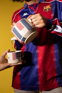 a woman is holding a cup of tea while wearing a fc barcelona shirt