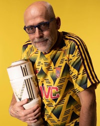 a bald man with glasses holding a soccer ball on a yellow background